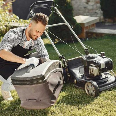 Man repairs lawnmover in a backyard